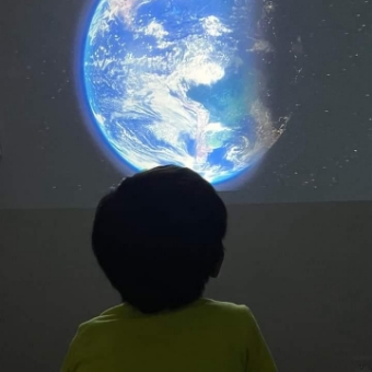 子どもが一人暗い部屋で壁に映し出された地球の映像を見ています