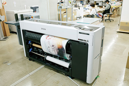 1F生産部工場内に設置、グレーインク搭載で6色機でも8色機同等の画質と色再現。長尺印刷や大量印刷時は、ダブルロールの用紙自動巻取り機能を使ってロールで保存。